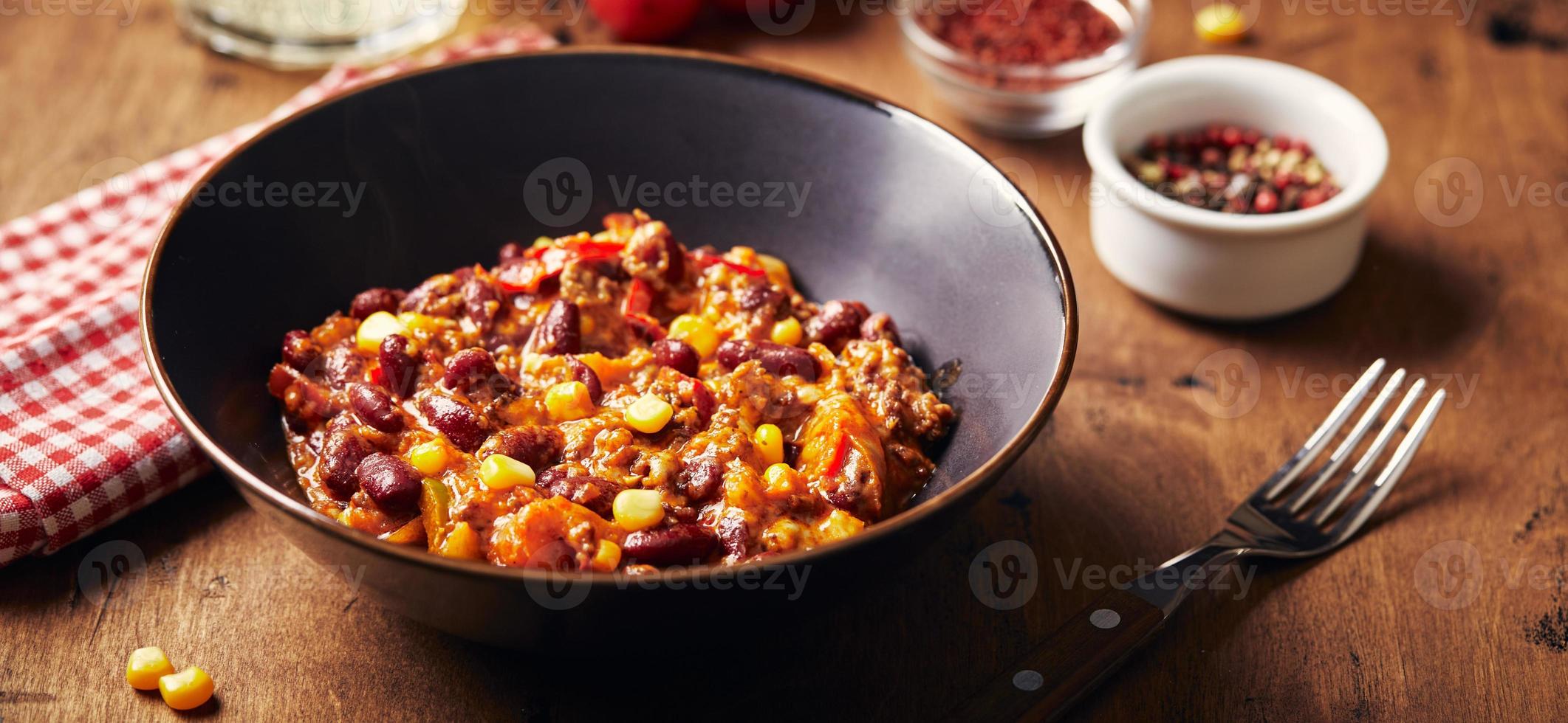 chili con carne con carne molida, frijoles y maíz en un tazón oscuro sobre fondo de madera. cocina mexicana y tejana foto