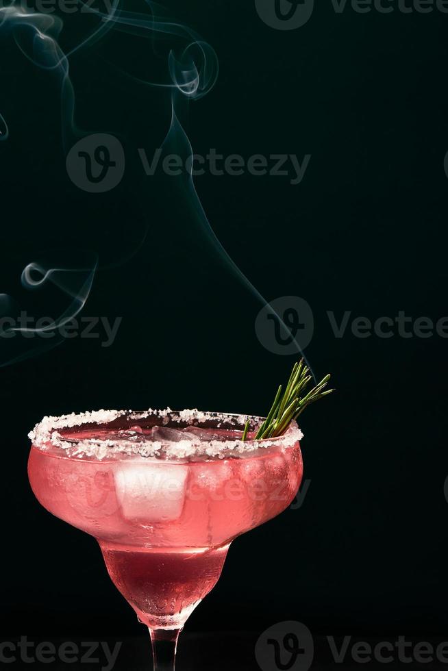 Alcoholic or non-alcoholic margarita type cocktail with ice and steaming rosemary branch on dark background photo