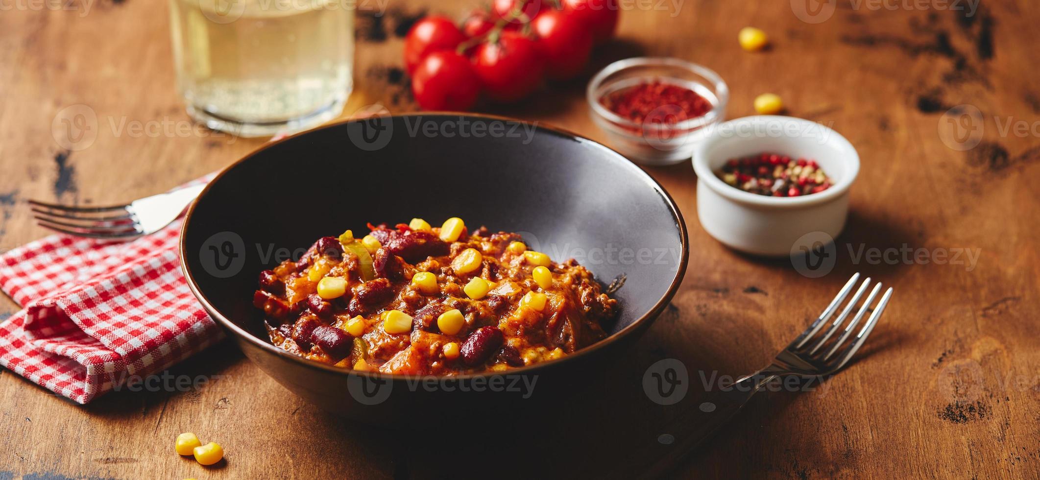 chili con carne con carne molida, frijoles y maíz en un tazón oscuro sobre fondo de madera. cocina mexicana y tejana foto