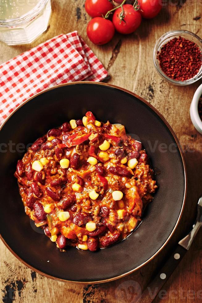 chili con carne con carne molida, frijoles y maíz en un tazón oscuro sobre fondo de madera. cocina mexicana y tejana foto