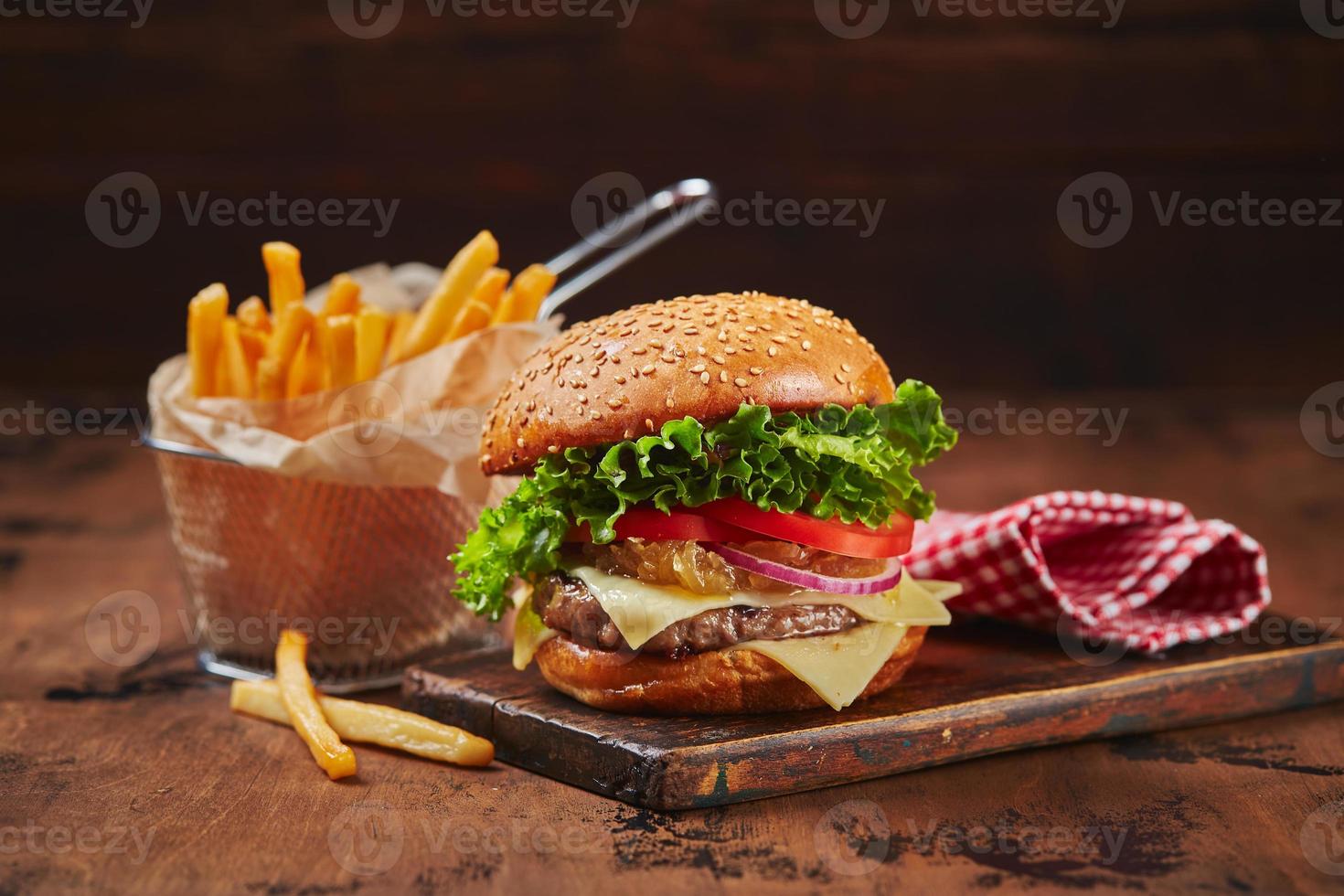 Homemade burger with beef, cheese and onion marmalade on a wooden board, fries in a metal basket. Fast food concept, american food photo