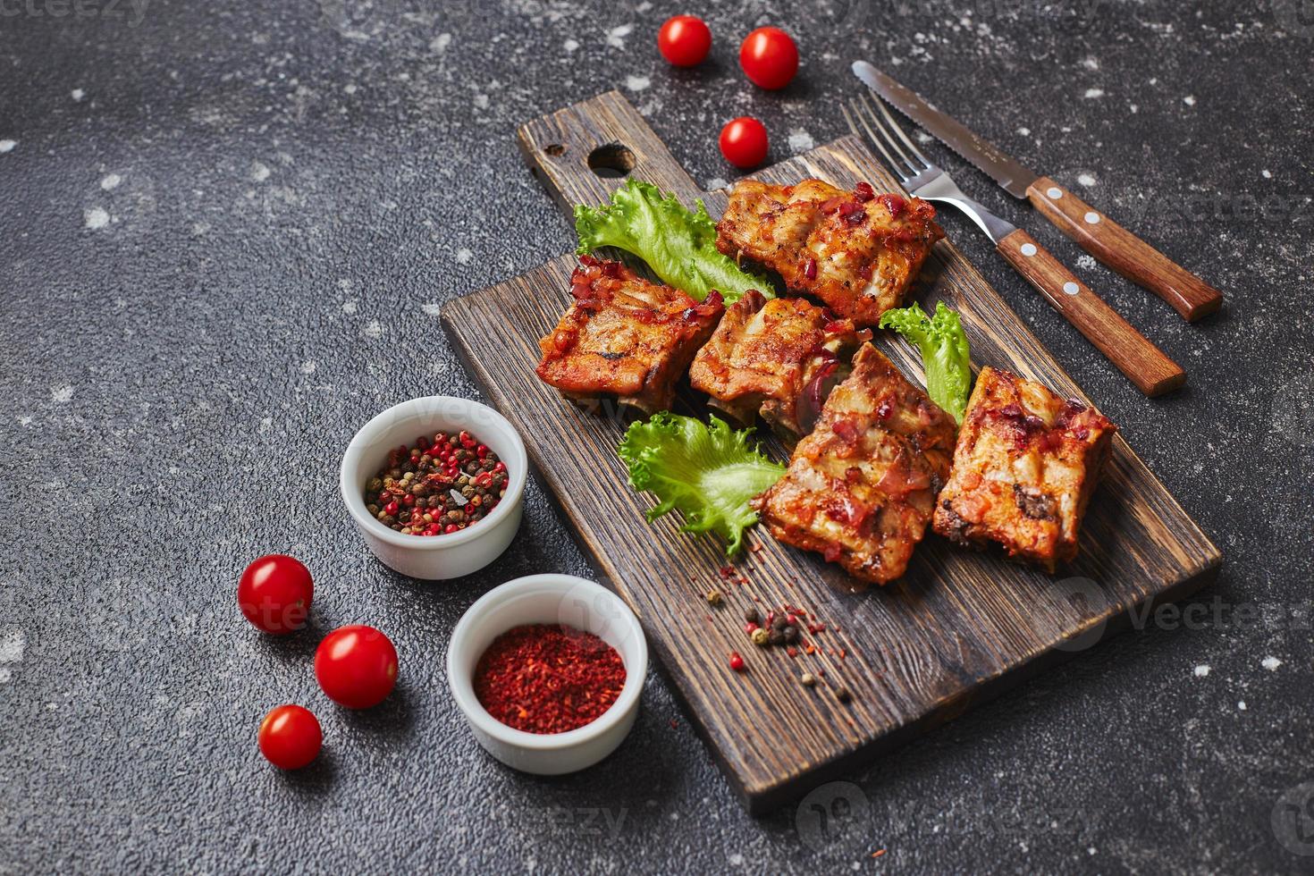 costillas de cerdo al horno a la parrilla con especias y verduras sobre tabla de cortar de madera sobre fondo oscuro. concepto de comida americana. foto