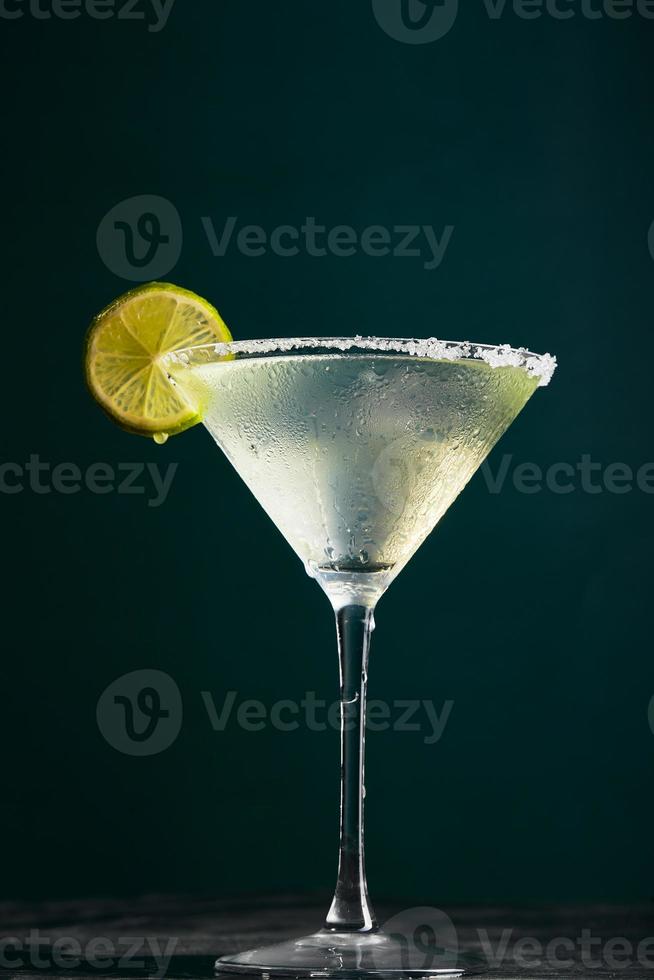 copa de martini con cóctel o cóctel sin alcohol y rodaja de lima sobre fondo oscuro foto