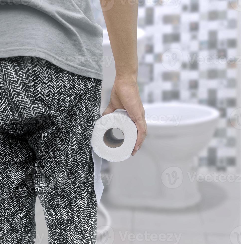 A person suffering from diarrhea holds a roll of toilet paper in front of the toilet bowl photo