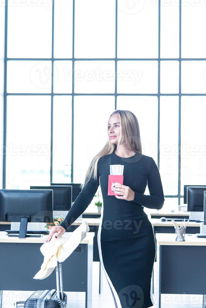 Tourist concept, Caucasian beautiful business woman with blue eyes, long hair hold the passport, air ticket, luggage and hat in the office prepare travel accessories for travelling in summer holiday photo