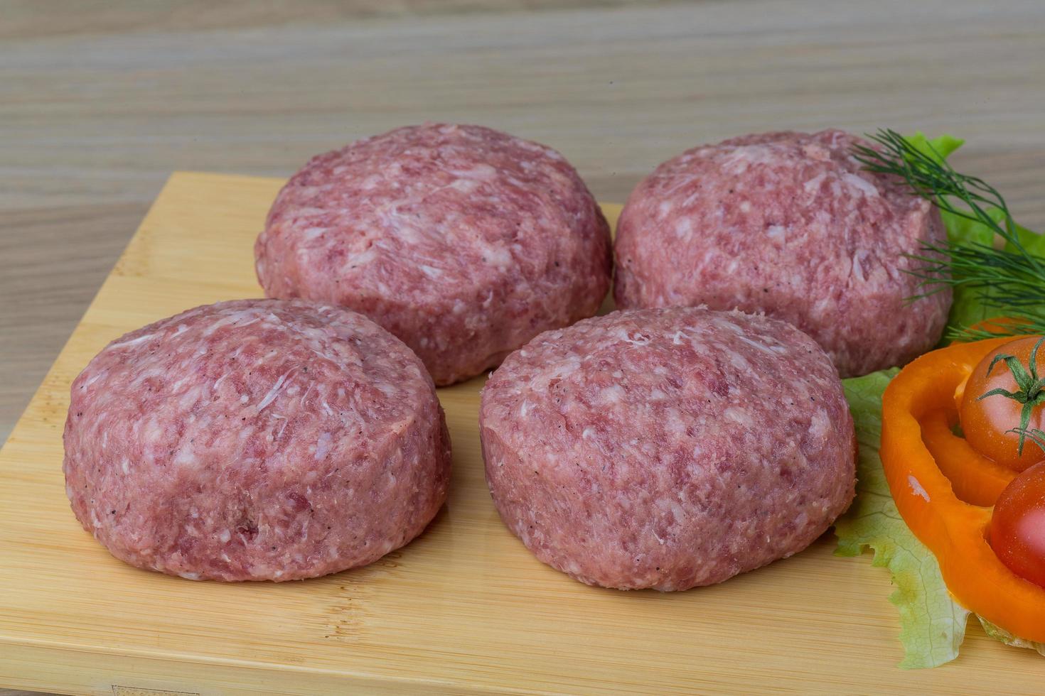 Raw burger cutlet on wooden board and wooden background photo