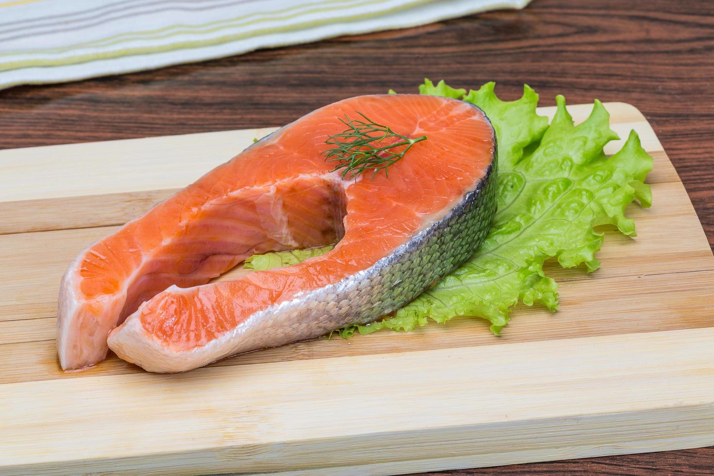Raw salmon steak on wooden board and wooden background photo