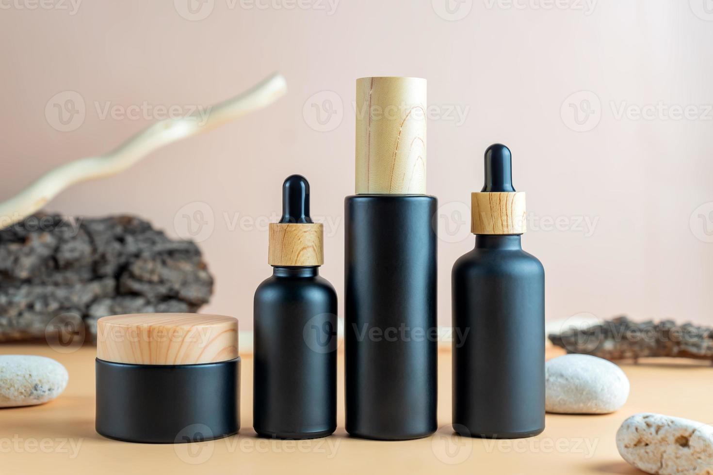 Set of natural cosmetics in black frosted glass packages on on beige background with bark of the tree, stones and wood branch. SPA natural organic beauty product packaging design photo