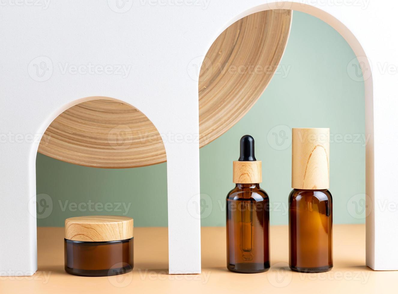 Amber glass dropper bottles and cream jar on white podiums arch. Beige background. Container mockup with cosmetic oil or serum. Showcase for the presentation skincare products photo