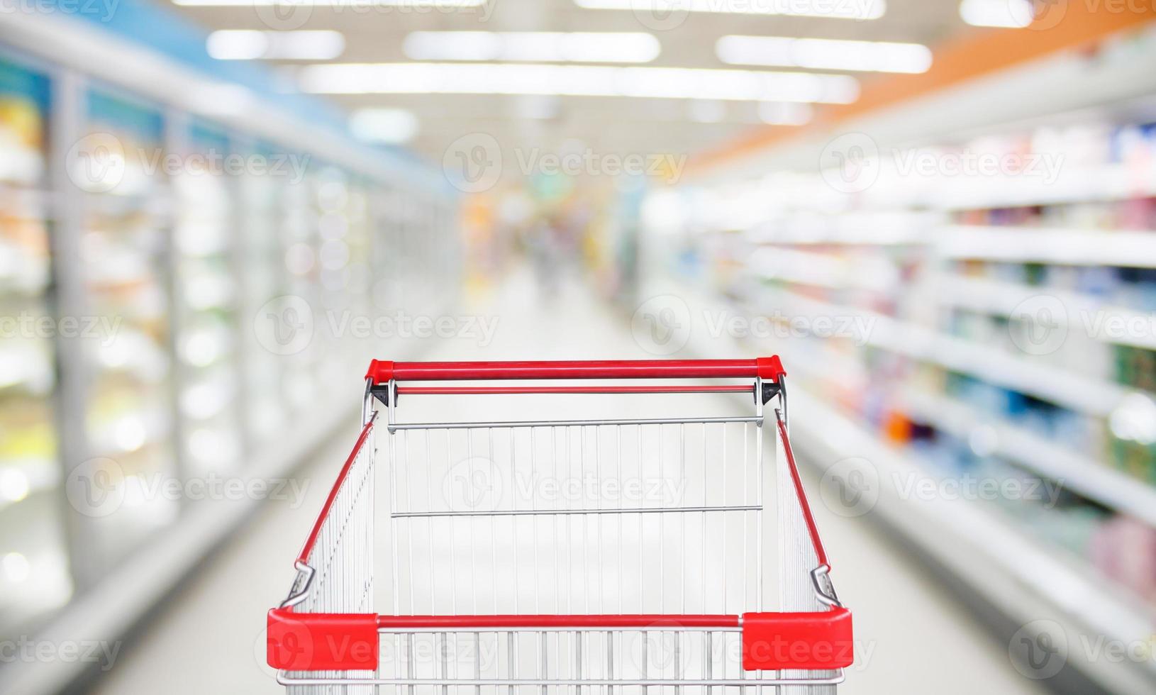 Supermarket aisle blur defocused background with empty red shopping cart photo