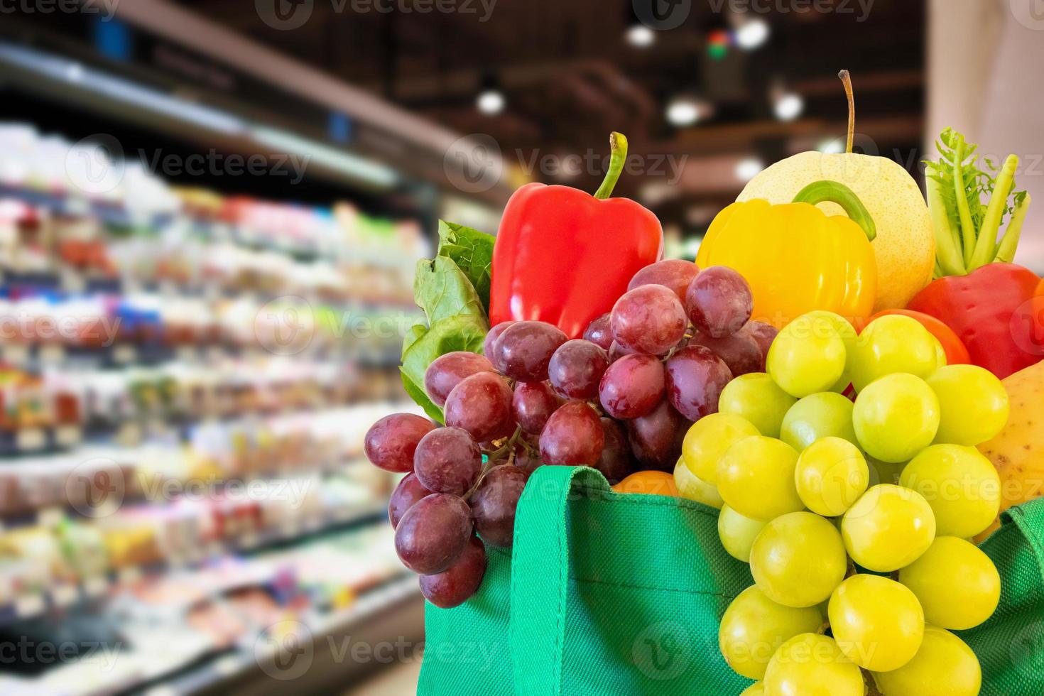 Fresh fruits and vegetables in reusable green shopping bag with supermarket grocery store blurred defocused background with bokeh light photo