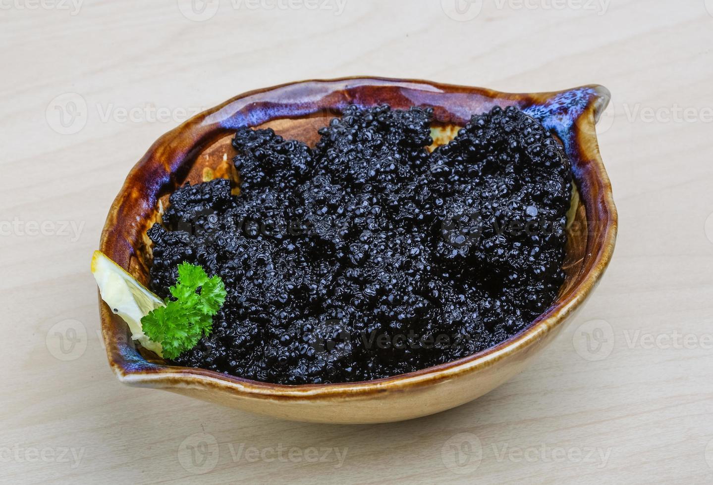 Black caviar in a bowl on wooden background photo