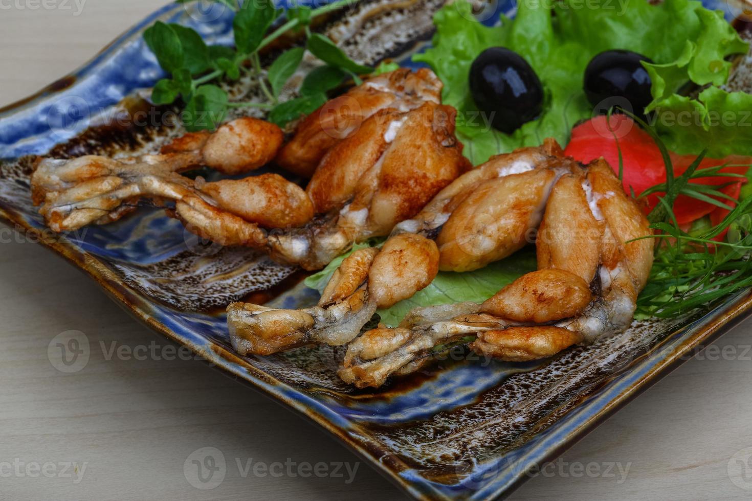 ancas de rana asadas en el plato y fondo de madera foto