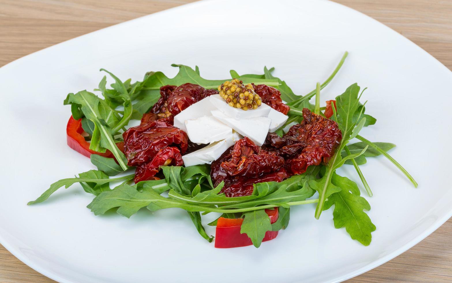 Salad with dried tomato on the plate and wooden background photo