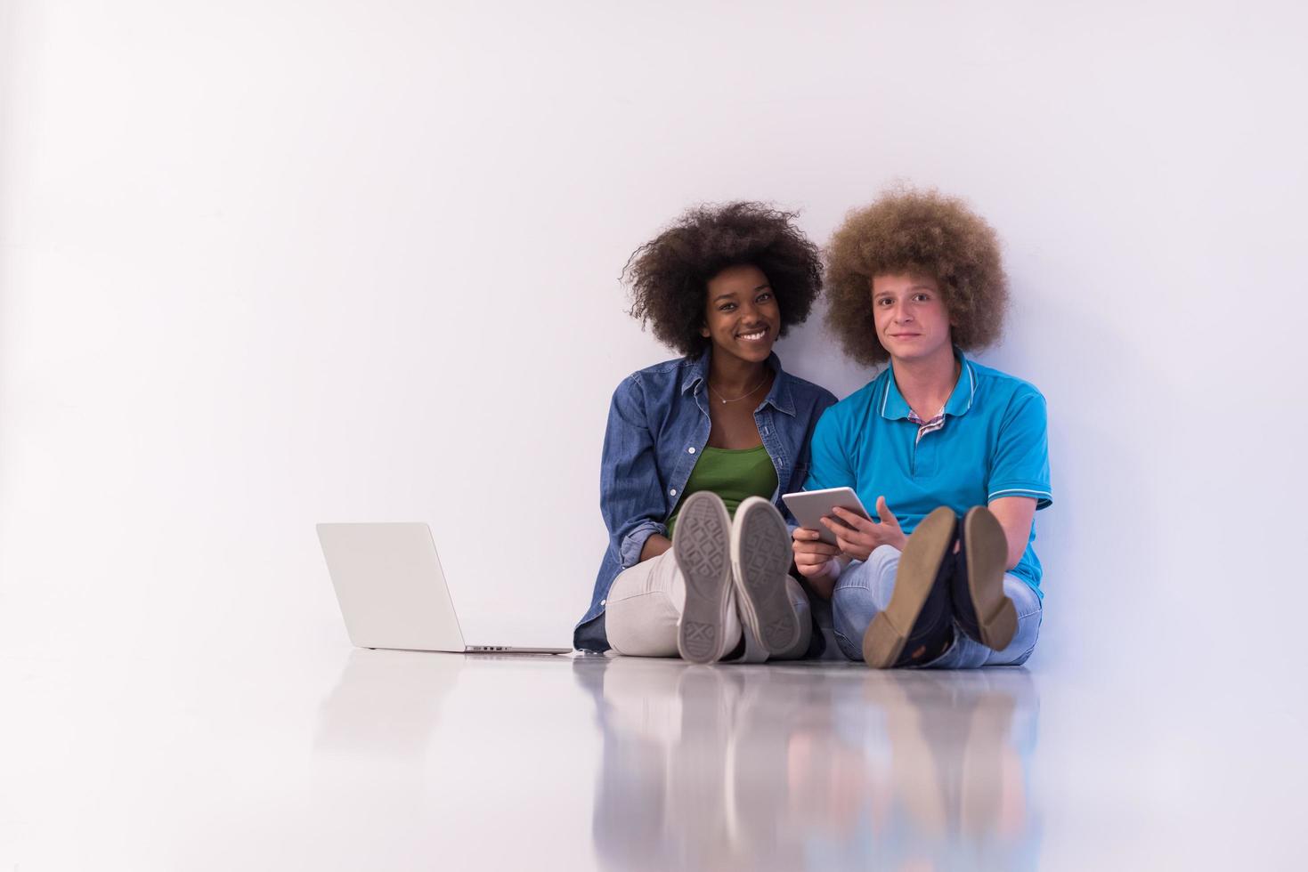 multiethnic couple sitting on the floor with a laptop and tablet photo