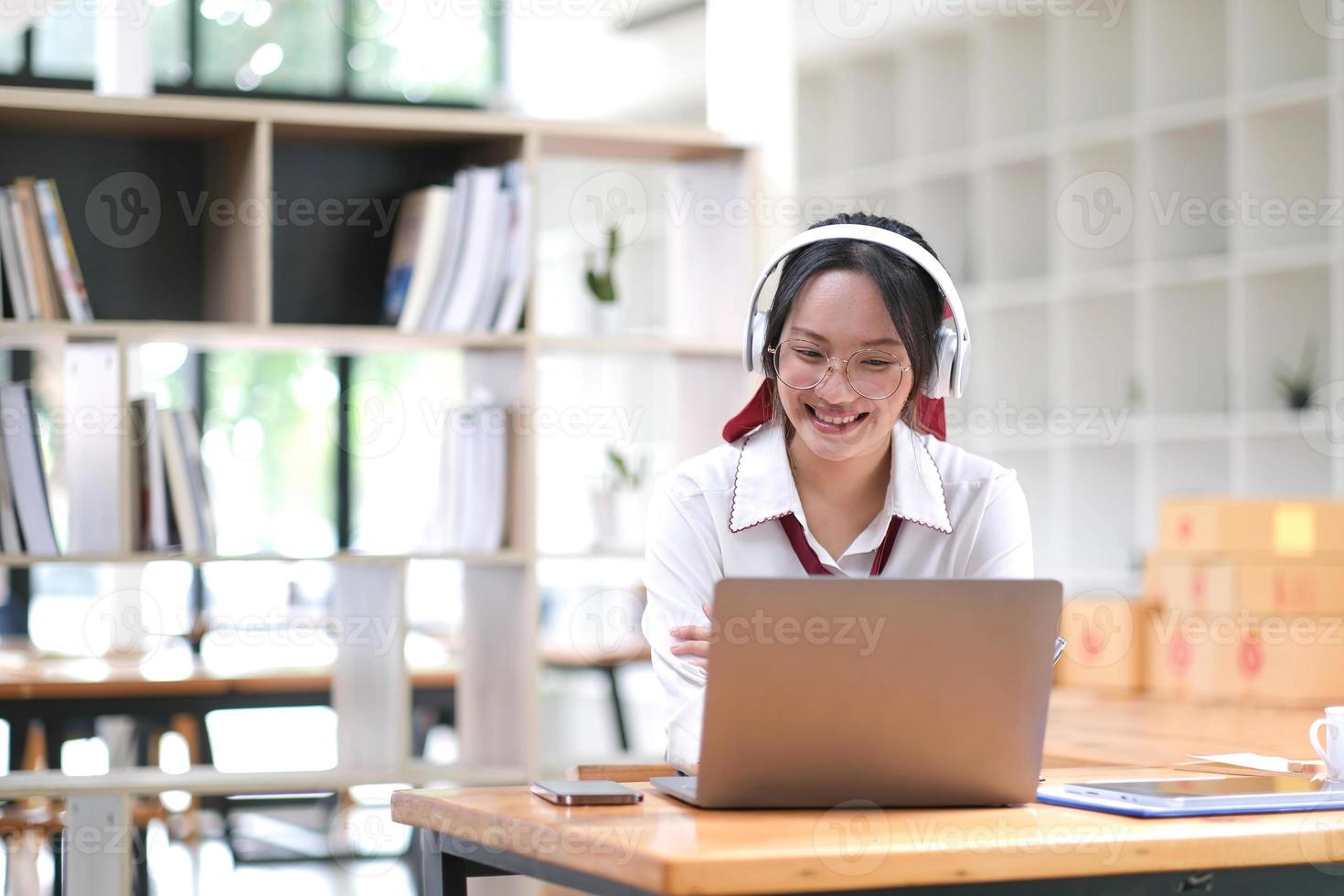 Young Asian woman student wearing headphones enjoy the convenience of using your laptop to study online at home interact with teachers effectively. photo