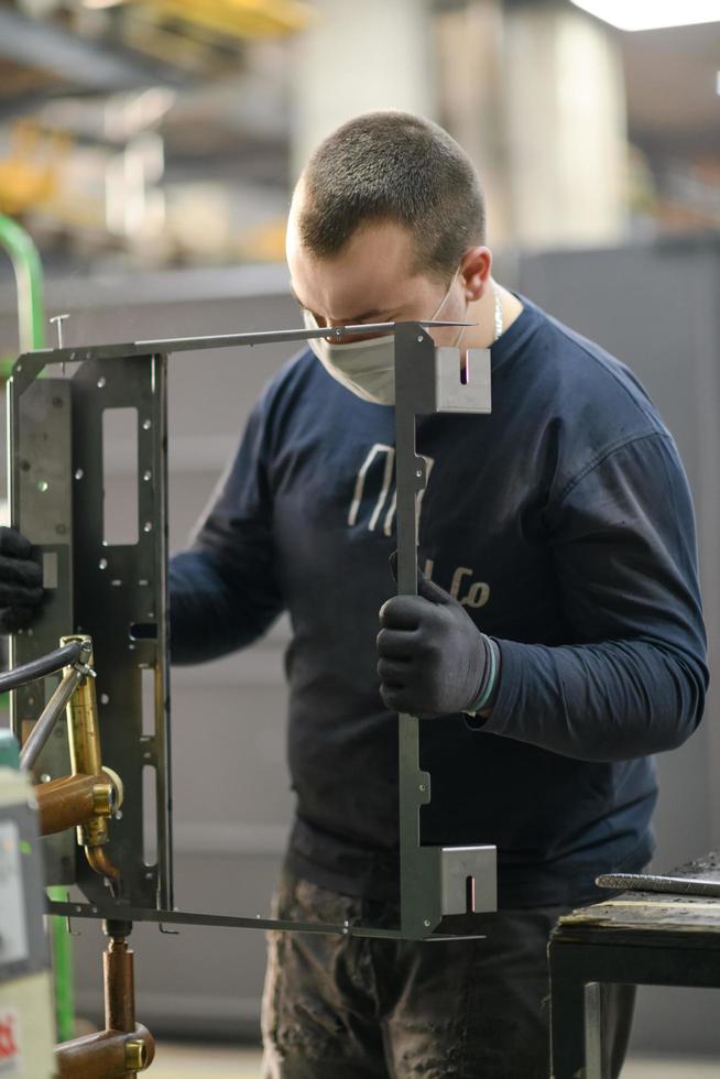 a uniformed worker working in a modern metal production and processing factory assembles parts of a new machine on his desk photo