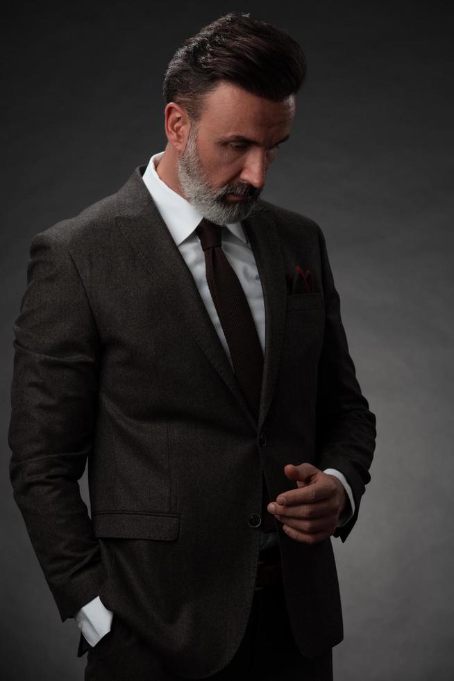 Portrait of a stylish elegant senior businessman with a beard and casual business clothes in photo studio isolated on dark background gesturing with hands