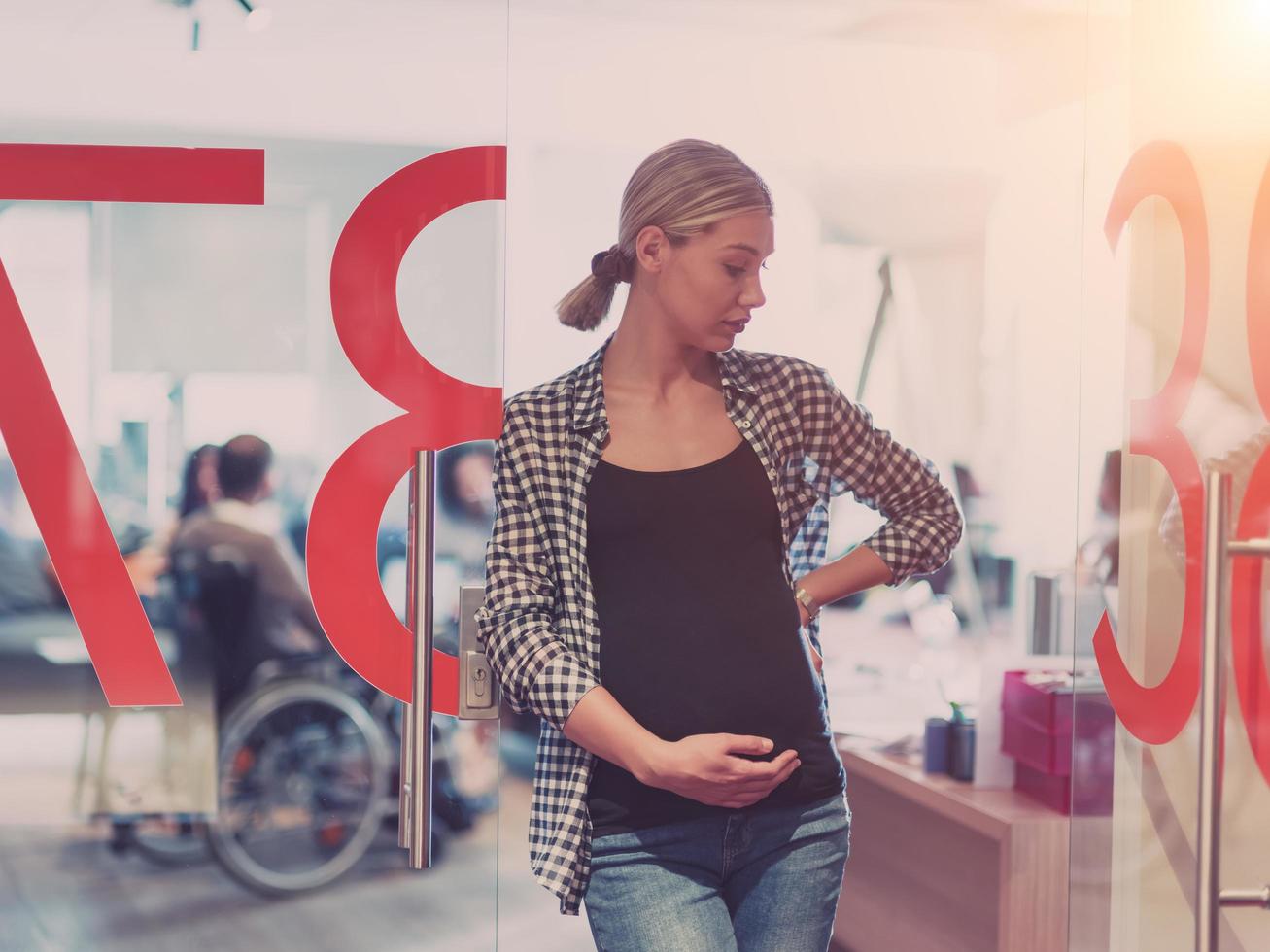 Portrait of pregnant businesswoman gently holding belly in modern office photo