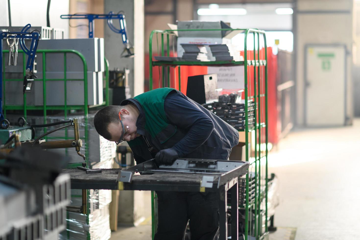 a uniformed worker working in a modern metal production and processing factory assembles parts of a new machine on his desk photo