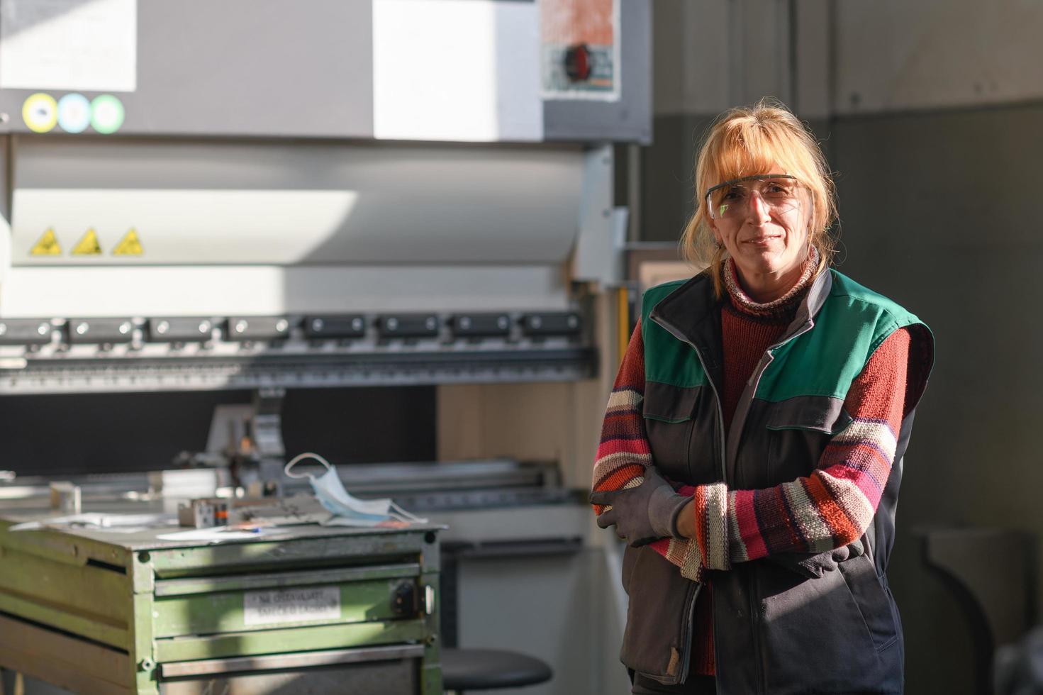 retrato de una mujer parada frente a una máquina cnc con gafas y trabajando en una moderna fábrica de producción y procesamiento de metales foto