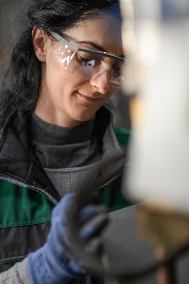 Woman worker wearing safety goggles control lathe machine to drill components. Metal lathe industrial manufacturing factory photo