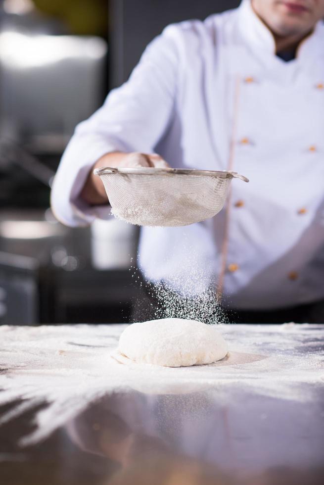 chef sprinkling flour over fresh pizza dough photo