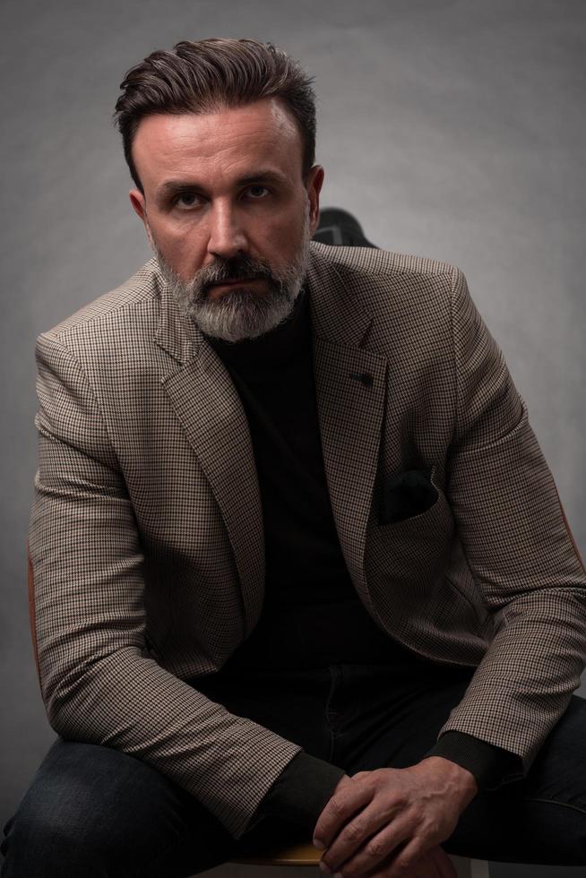 Portrait of a stylish elegant senior businessman with a beard and casual business clothes in photo studio isolated on dark background gesturing with hands