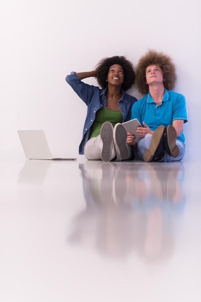 multiethnic couple sitting on the floor with a laptop and tablet photo