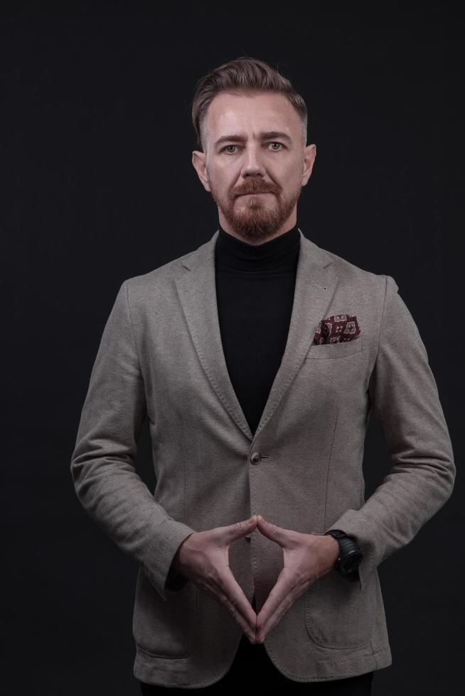 Portrait of a stylish elegant senior businessman with a beard and casual business clothes in photo studio isolated on dark background gesturing with hands