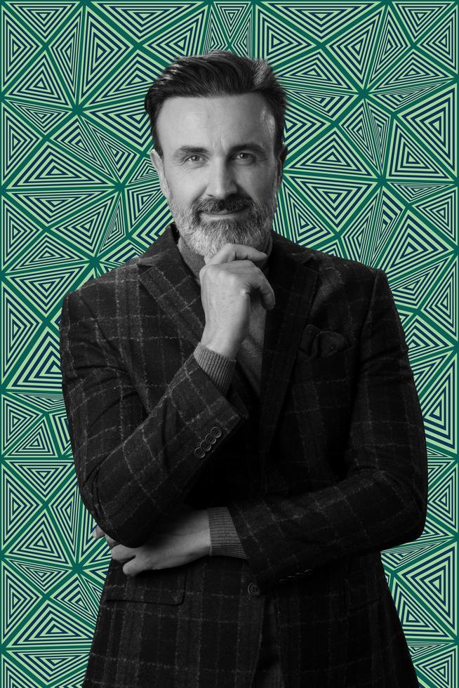 Black and white portrait of a stylish elegant senior businessman with a beard and casual business clothes against retro colorful pattern design background gesturing with hands photo