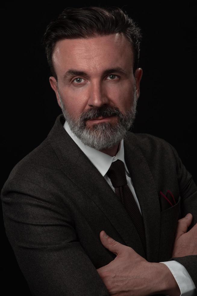 Portrait of a stylish elegant senior businessman with a beard and casual business clothes in photo studio isolated on dark background gesturing with hands