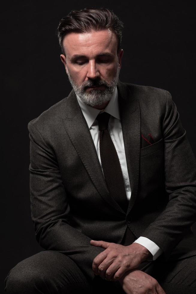 Portrait of a stylish elegant senior businessman with a beard and casual business clothes in photo studio isolated on dark background gesturing with hands