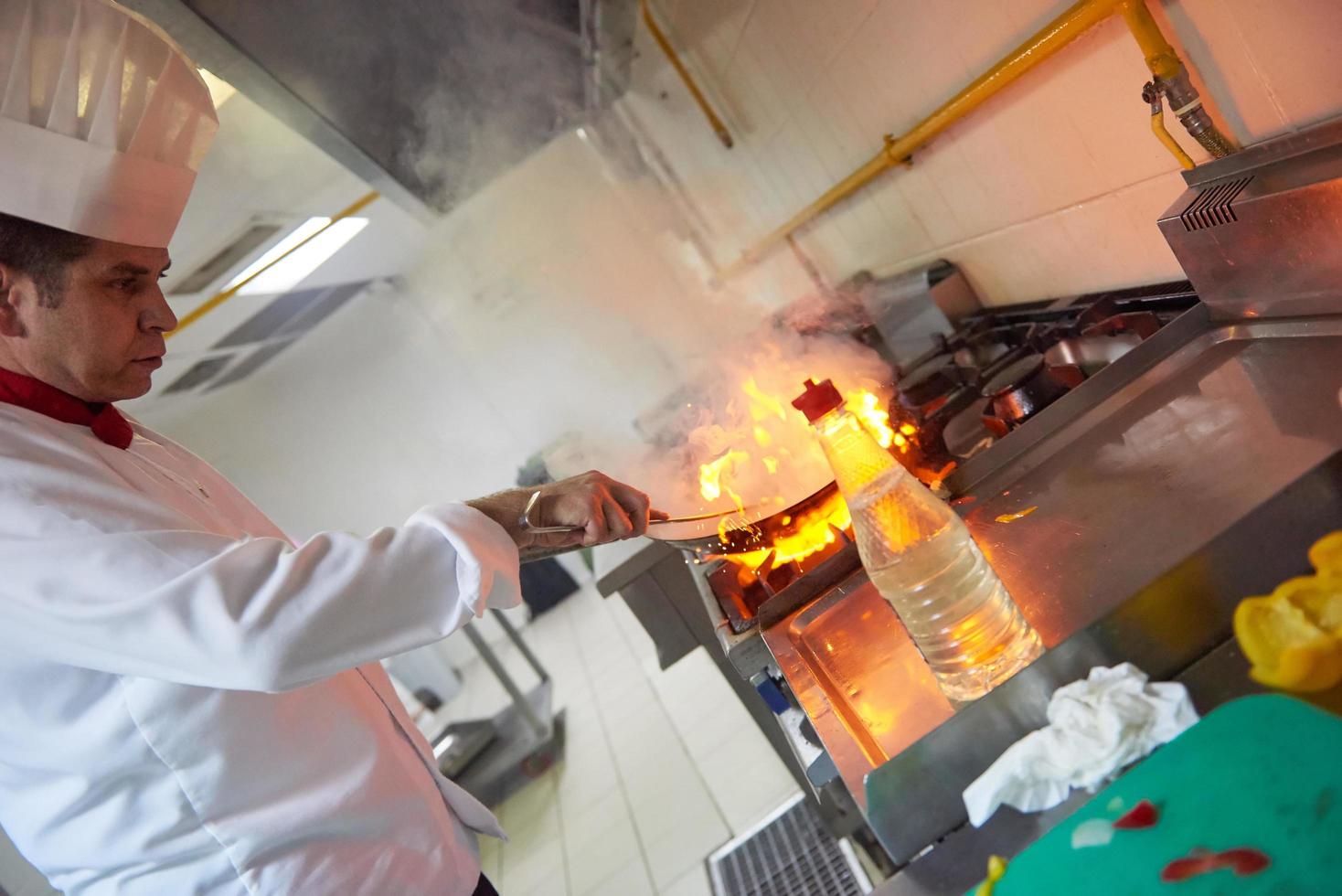 chef en la cocina del hotel prepara comida con fuego foto