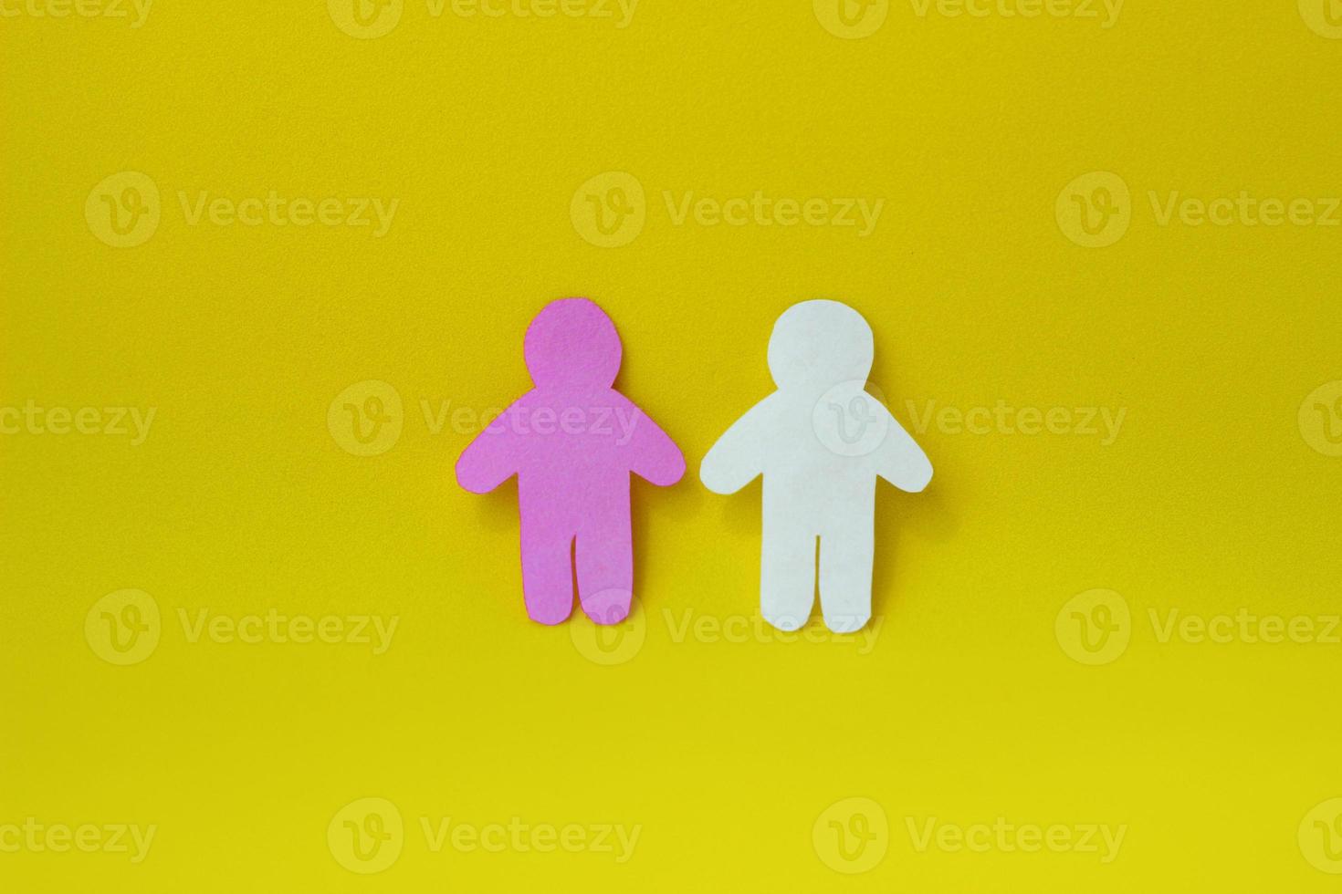 Two silhouettes of a people carved from white and pink paper on yellow background. photo