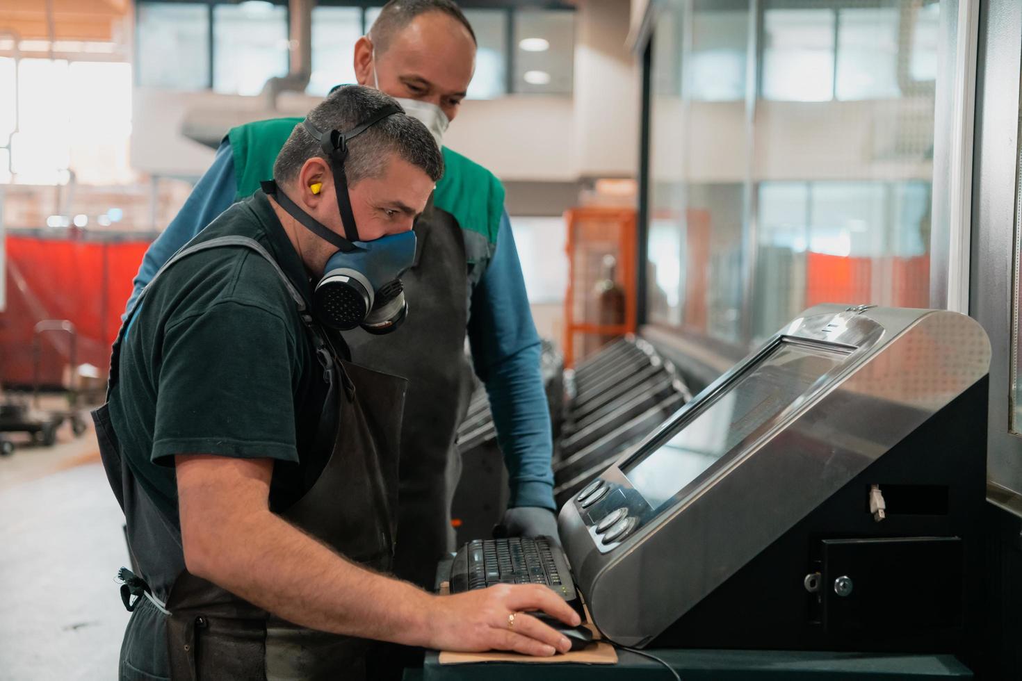 two workers wearing a face mask due to a coronavirus pandemic are programming a modern cnc machine photo