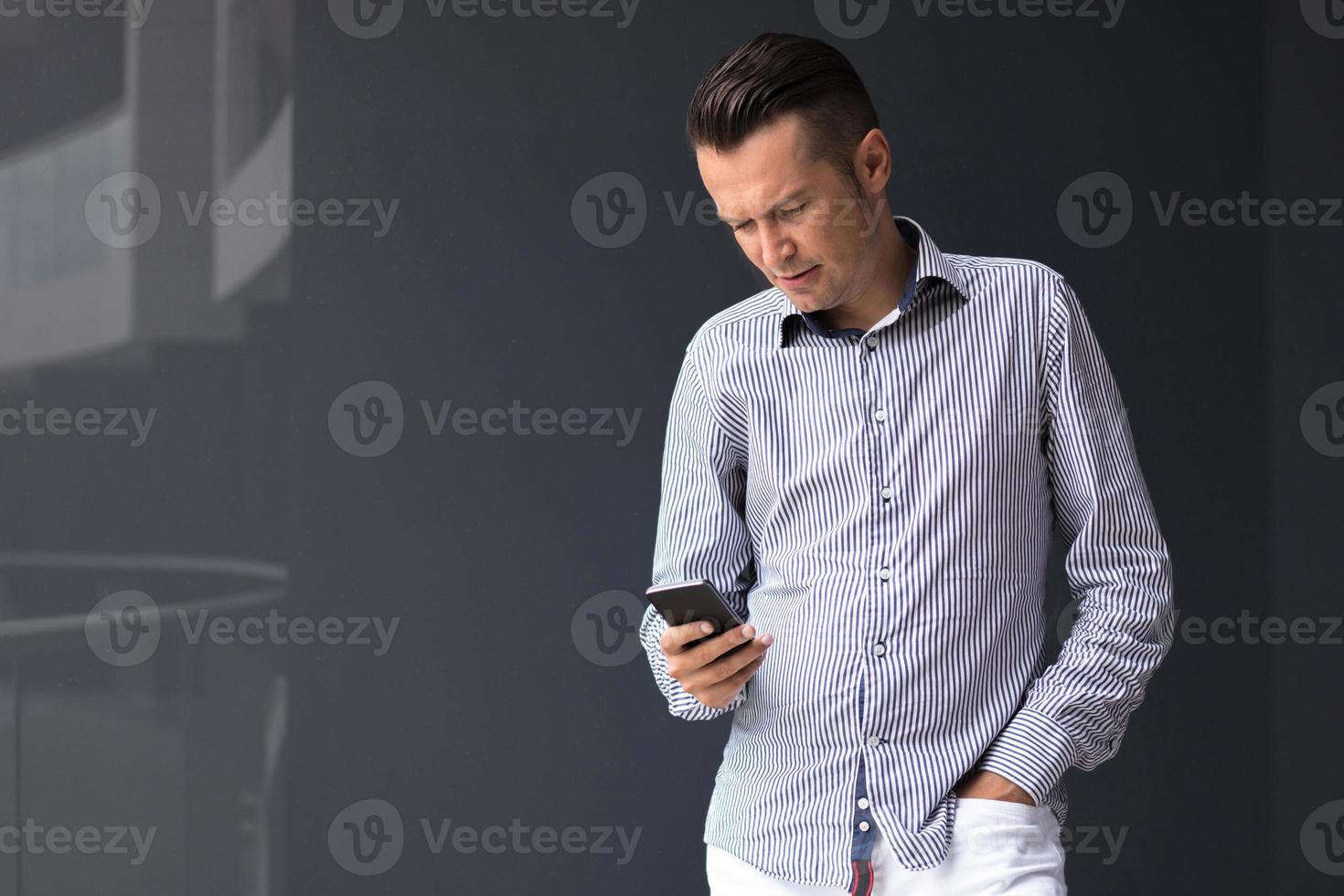 Businessman text messaging on mobile phone against the wall. photo
