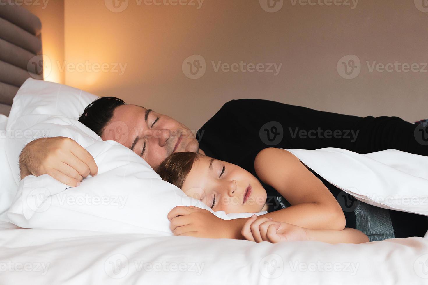 Father and son sleeping on a bed together. photo