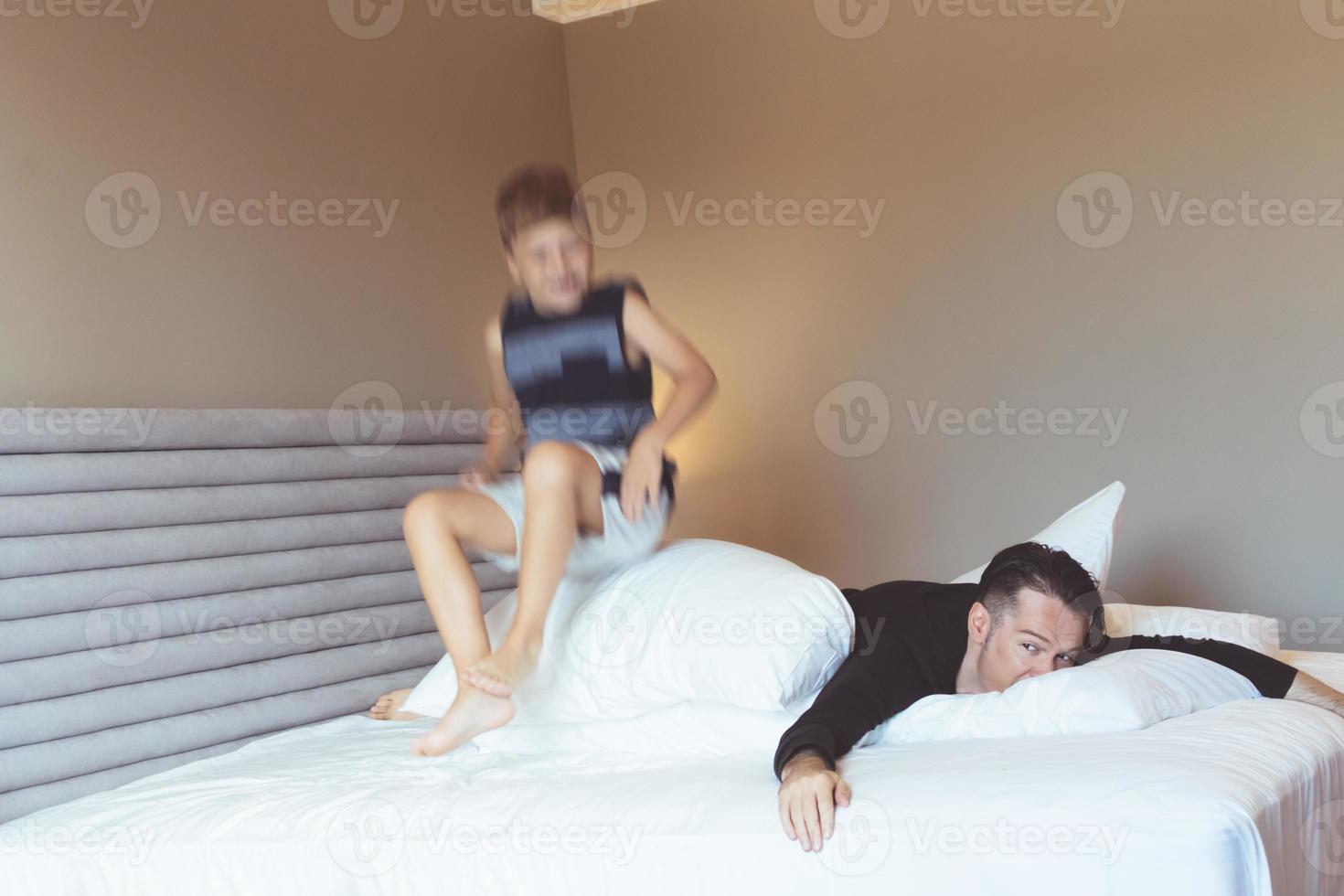 Boy in blurred motion jumping on the bed while playing with is father. photo