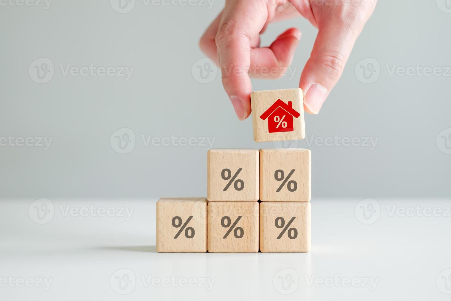 House and property investment and asset management concept. Interest rates, loan mortgage, house tax. Hand holding house icon with percent sign from stack of blocks with percentage icon photo