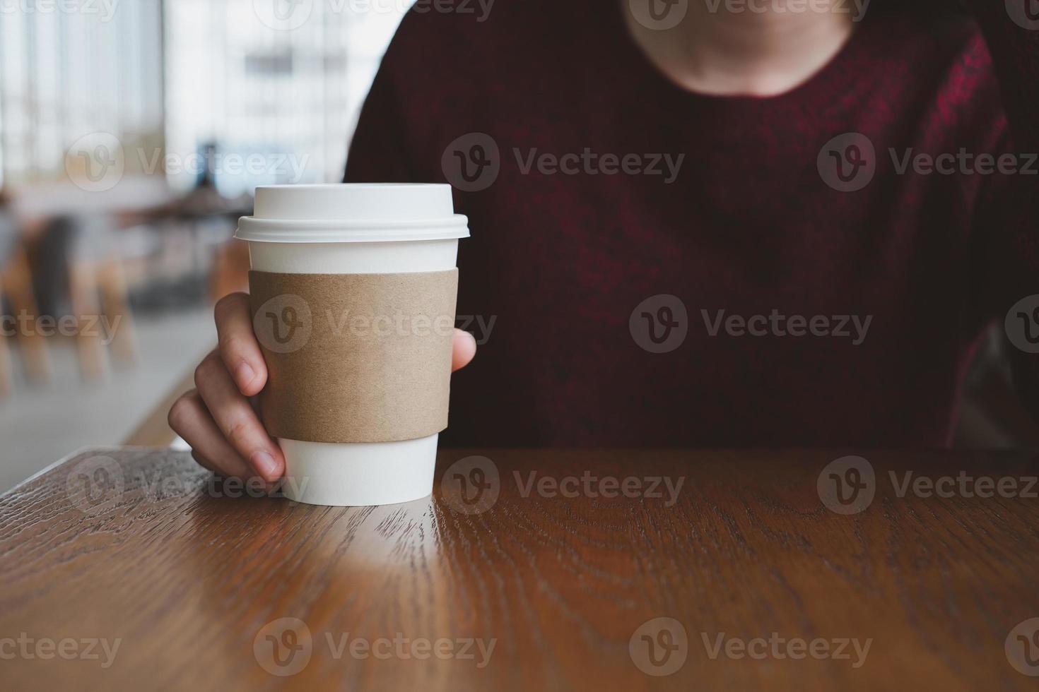 mano de mujer sosteniendo una taza de papel blanco de café caliente en la cafetería. foto