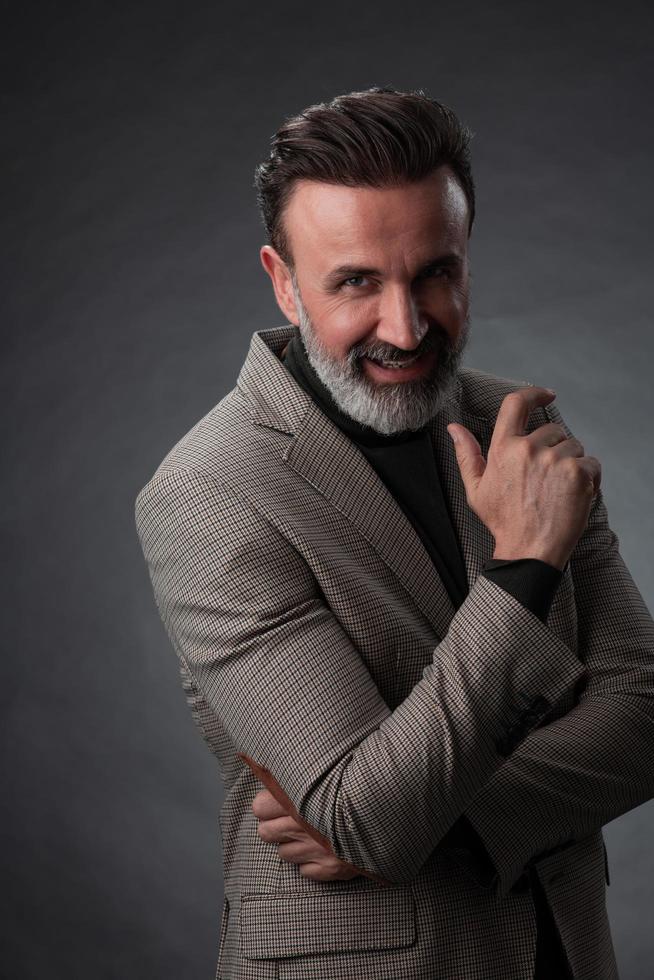 Portrait of a stylish elegant senior businessman with a beard and casual business clothes in photo studio isolated on dark background gesturing with hands