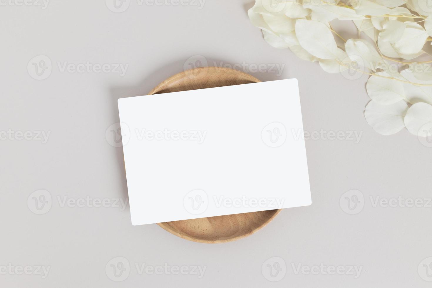 Greeting card or invitation card with white dry flower leaves on wood plate or tray in beige background photo