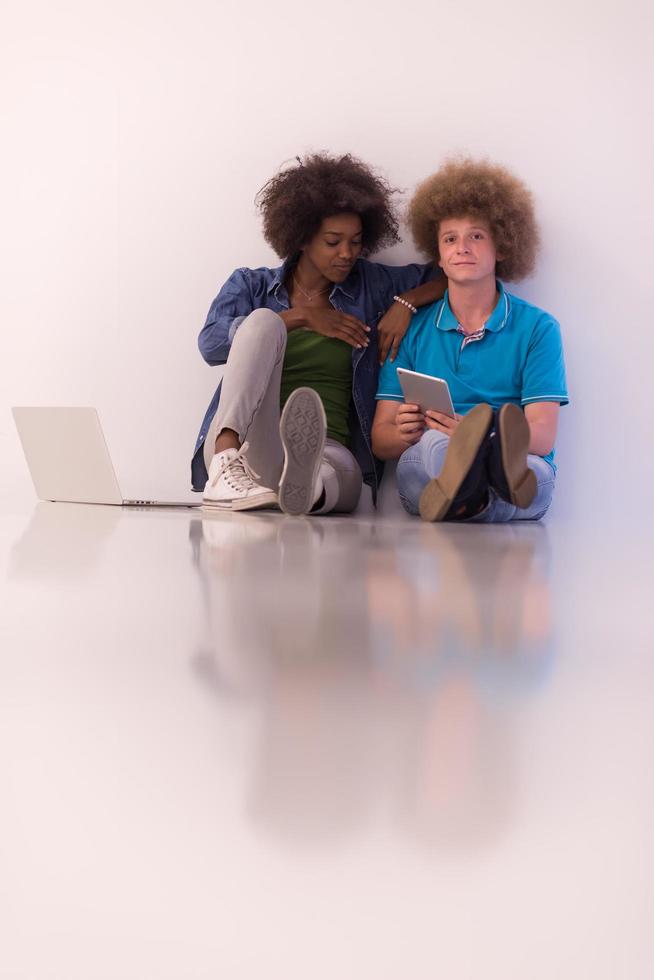 pareja multiétnica sentada en el suelo con una laptop y una tableta foto