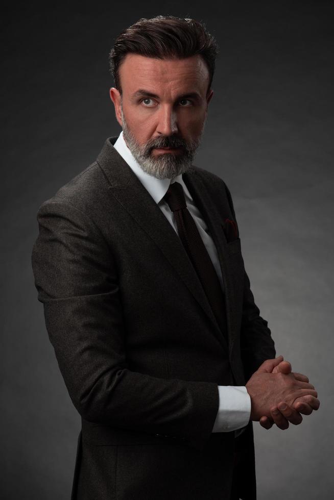 Portrait of a stylish elegant senior businessman with a beard and casual business clothes in photo studio isolated on dark background gesturing with hands