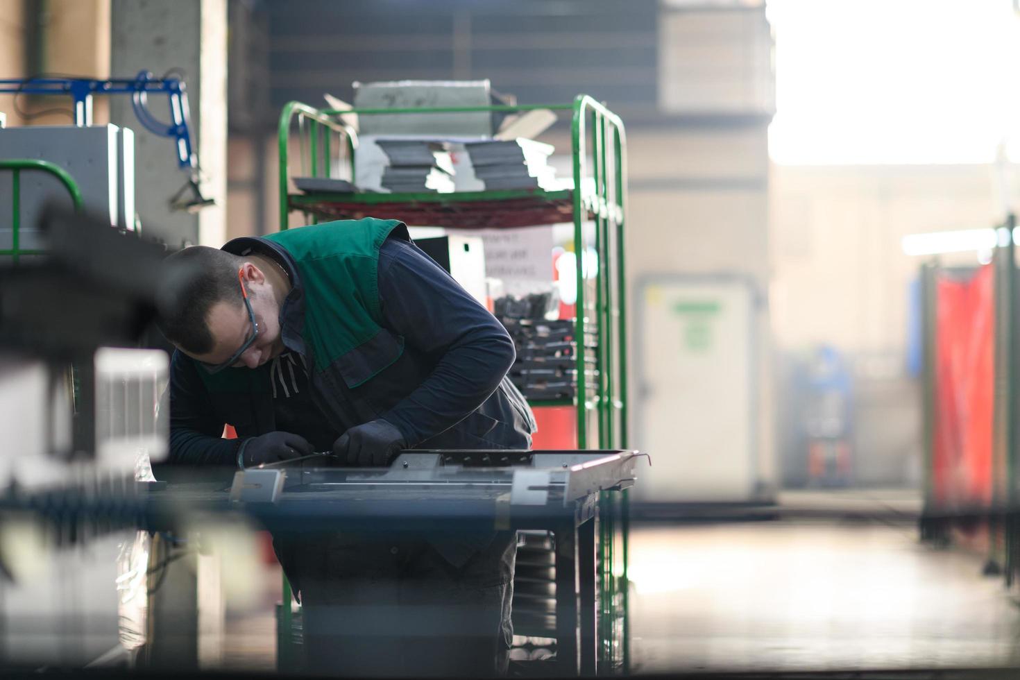 a uniformed worker working in a modern metal production and processing factory assembles parts of a new machine on his desk photo