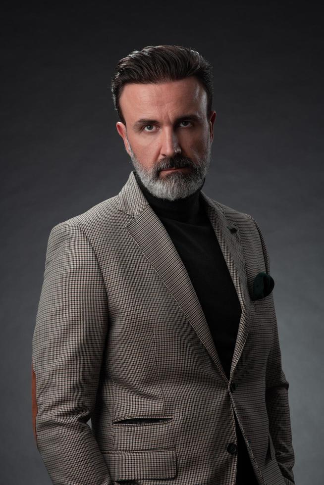 retrato de un elegante hombre de negocios de alto nivel con barba y ropa informal de negocios en un estudio fotográfico aislado en un fondo oscuro gesticulando con las manos foto