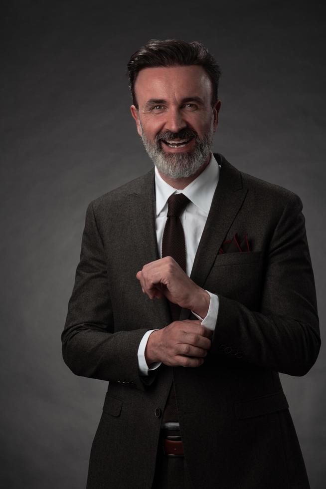 Portrait of a stylish elegant senior businessman with a beard and casual business clothes in photo studio adjusting suit