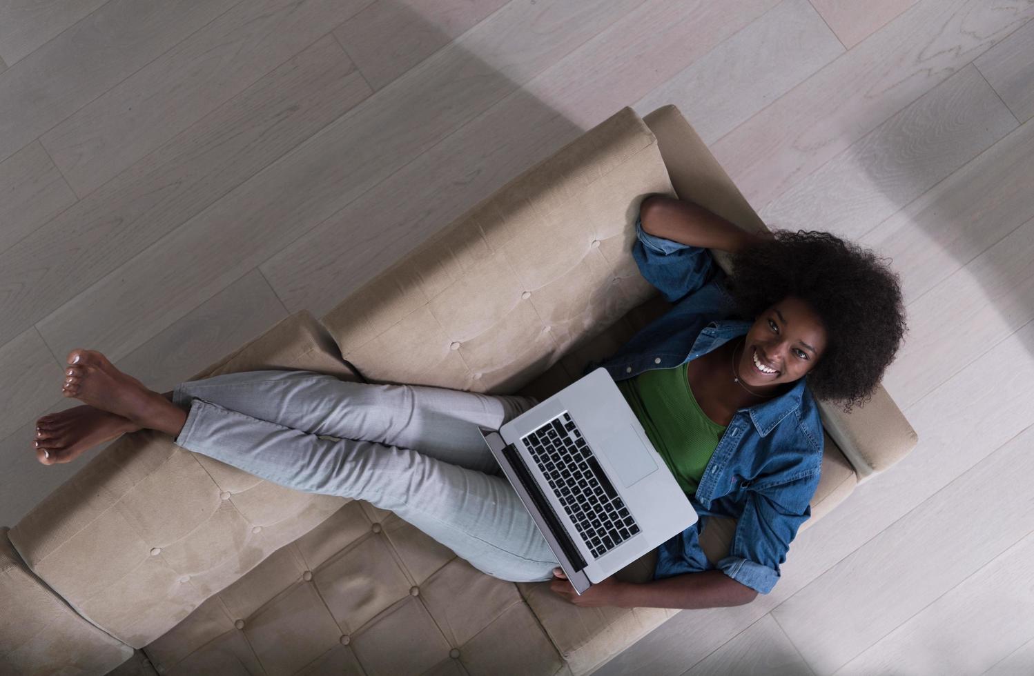 mujer afroamericana que usa la computadora portátil en la vista superior del sofá foto