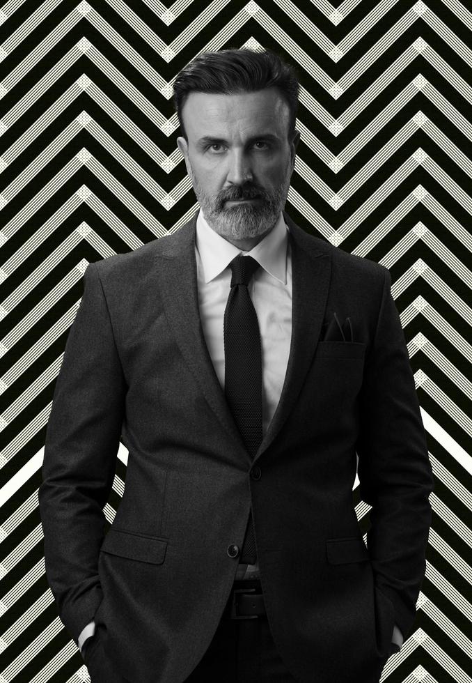 Black and white portrait of a stylish elegant senior businessman with a beard and casual business clothes against retro colorful pattern design background gesturing with hands photo